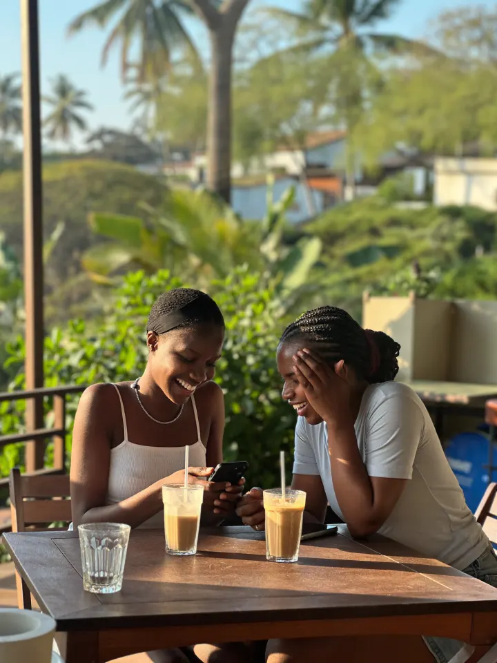 Two friends at a café table laughing at something on a phone