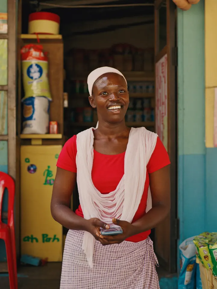 A shopkeeper standing in the doorway of her corner store with her phone